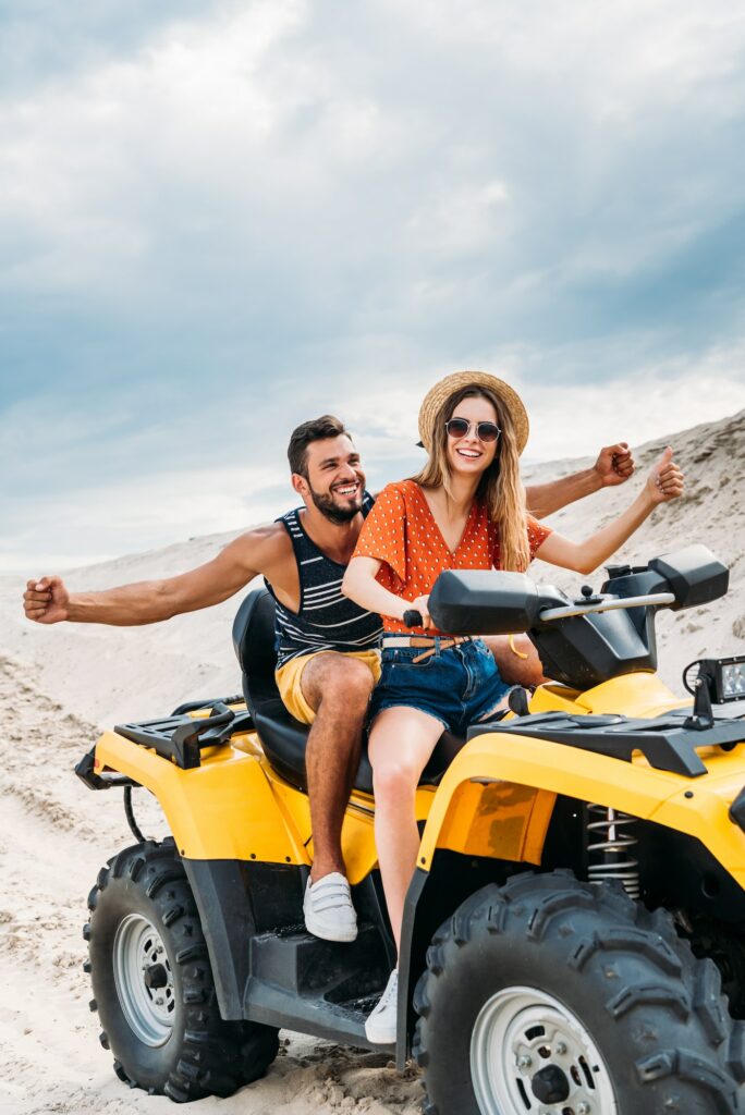 happy young couple riding all-terrain vehicle in desert on cloudy day